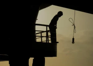 A silhouette of a person standing on a balcony at sunset with a hanging light bulb in view.