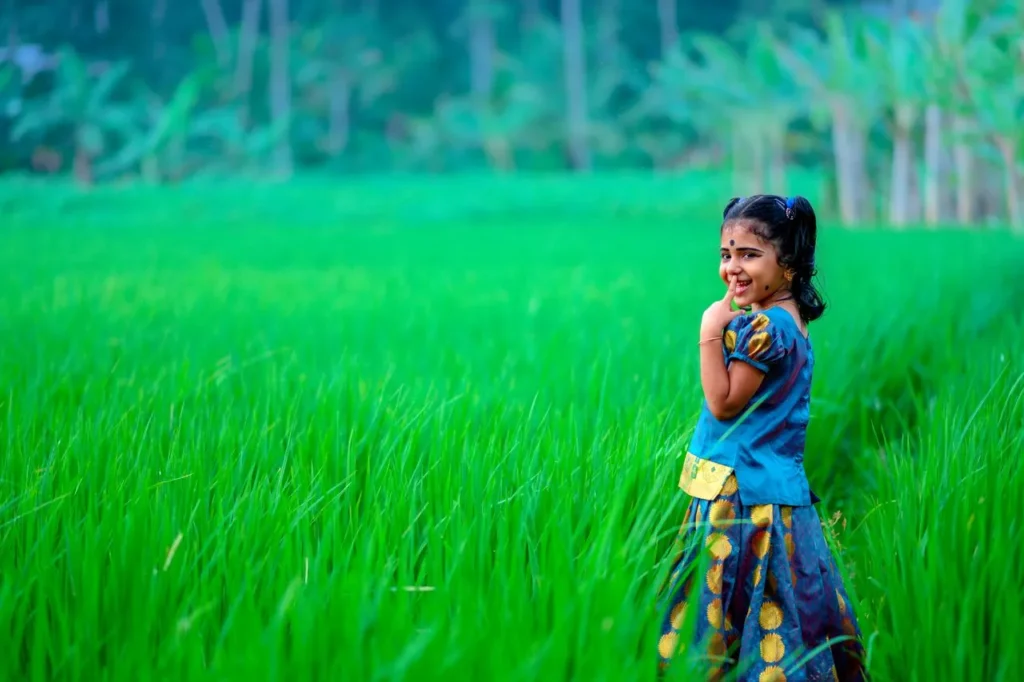 A young girl joyfully poses in a vibrant green field, embodying the spirit of Kerala's countryside.
